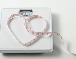 A bathroom scale with a tape measure forming a heart shape on it.
