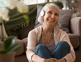 A smiling woman sitting on the floor in a living room with headphones on.