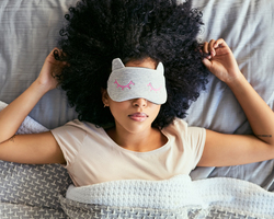 A woman lies in bed with a sleep mask over her eyes. 