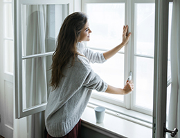 A woman holds the latch of a window.