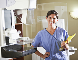 A mammogram technician standing next to a mammogram machine.
