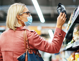 A woman wearing a face mask looks at a package label in a grocery store.