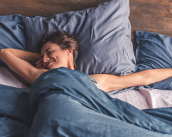 A smiling woman stretches as she lies in bed.