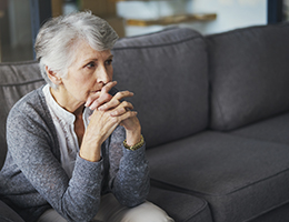 An older woman sits on a couch looking sad.