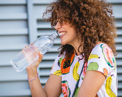 A smiling woman drinks from a water bottle.