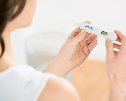 A woman, seen from behind, holds a pregnancy test in both hands.