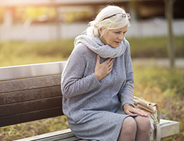 A woman sitting on a bench with her hand over her heart.