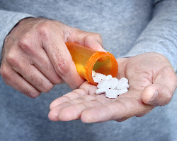 Close-up on man’s hands pouring white tablets from a pill bottle into his palm.
