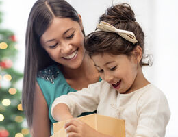 A child unboxes a gift while a smiling woman looks on.