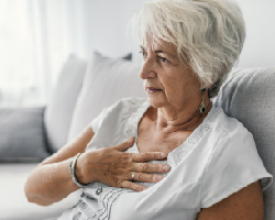 An older woman presses her hand to her chest. 