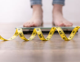 Close-up of measuring tape in front of feet on a bathroom scale