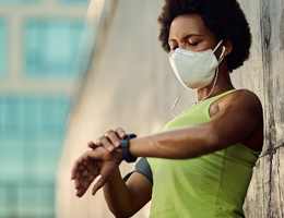 A masked woman wearing a tank top looks at her watch.