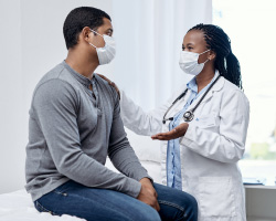 A masked patient talks to a masked doctor.