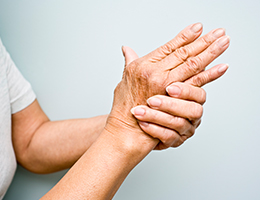A woman with arthritic hands is gripping one hand with the other.