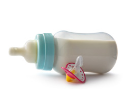 A full baby bottle on its side next to a pacifier.